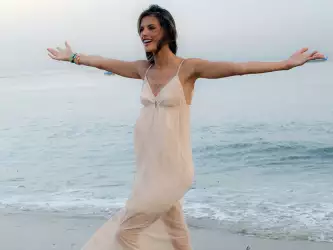 Alessandra Ambrosio gracefully strolling on the beach in a long white dress