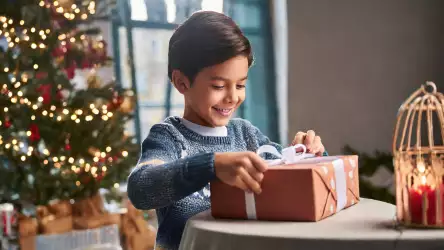 A boy joyfully unwrapping a Christmas gift, his face lit up with excitement and surprise