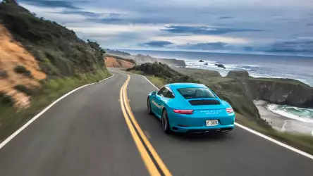 Blue Porsche Carrera gracefully driving on a hillside road, surrounded by scenic beauty