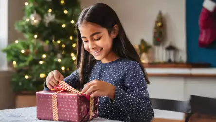 Illustration of a girl with a bright smile, eagerly unwrapping her Christmas present, capturing the magical moment of surprise and delight